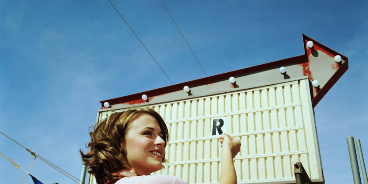 Woman holding letter 'R' in air, against empty sign, side view